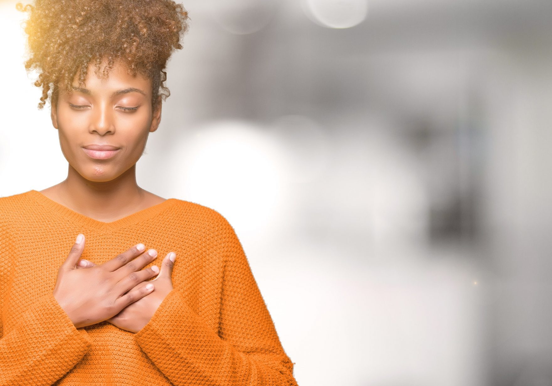 Woman wearing an orange sweater putting her hands over her heart